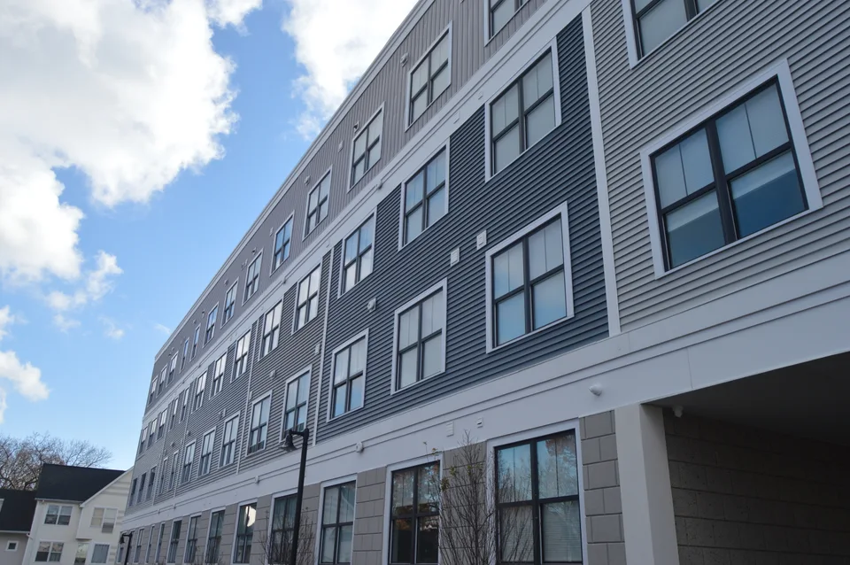 Multi-story building with gray horizontal siding, rows of windows and contrasting white trim.