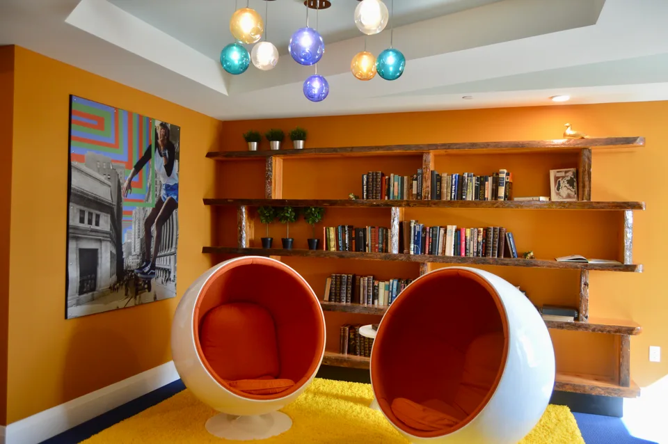 Open shelving filled with books behind two red chairs in a shared interior space.