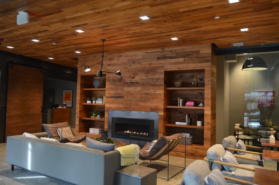 Lounge with wood ceiling planks and shelving around a fireplace and television.