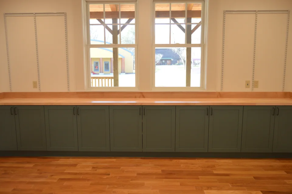 Cabinetry with a wood countertop beneath two trimmed windows.
