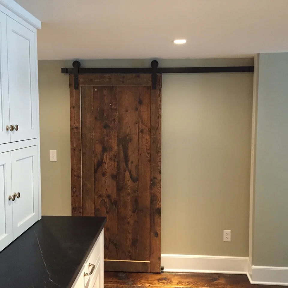 Wood sliding door on a black track beside white cabinetry and baseboard trim.