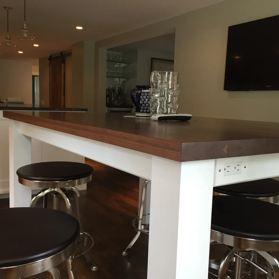 Wood-topped bar counter with white supports, seating and cabinets behind.