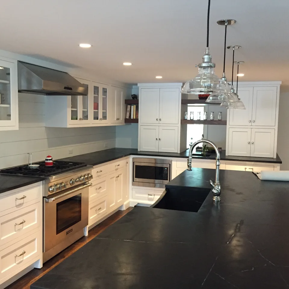 White kitchen cabinetry, glazed upper cabinets and dark countertops around a kitchen island.