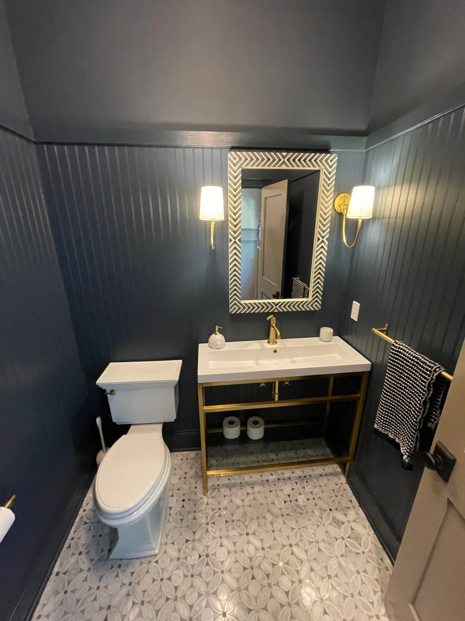 Dark vertical wall paneling and crown molding around a bathroom mirror and vanity.