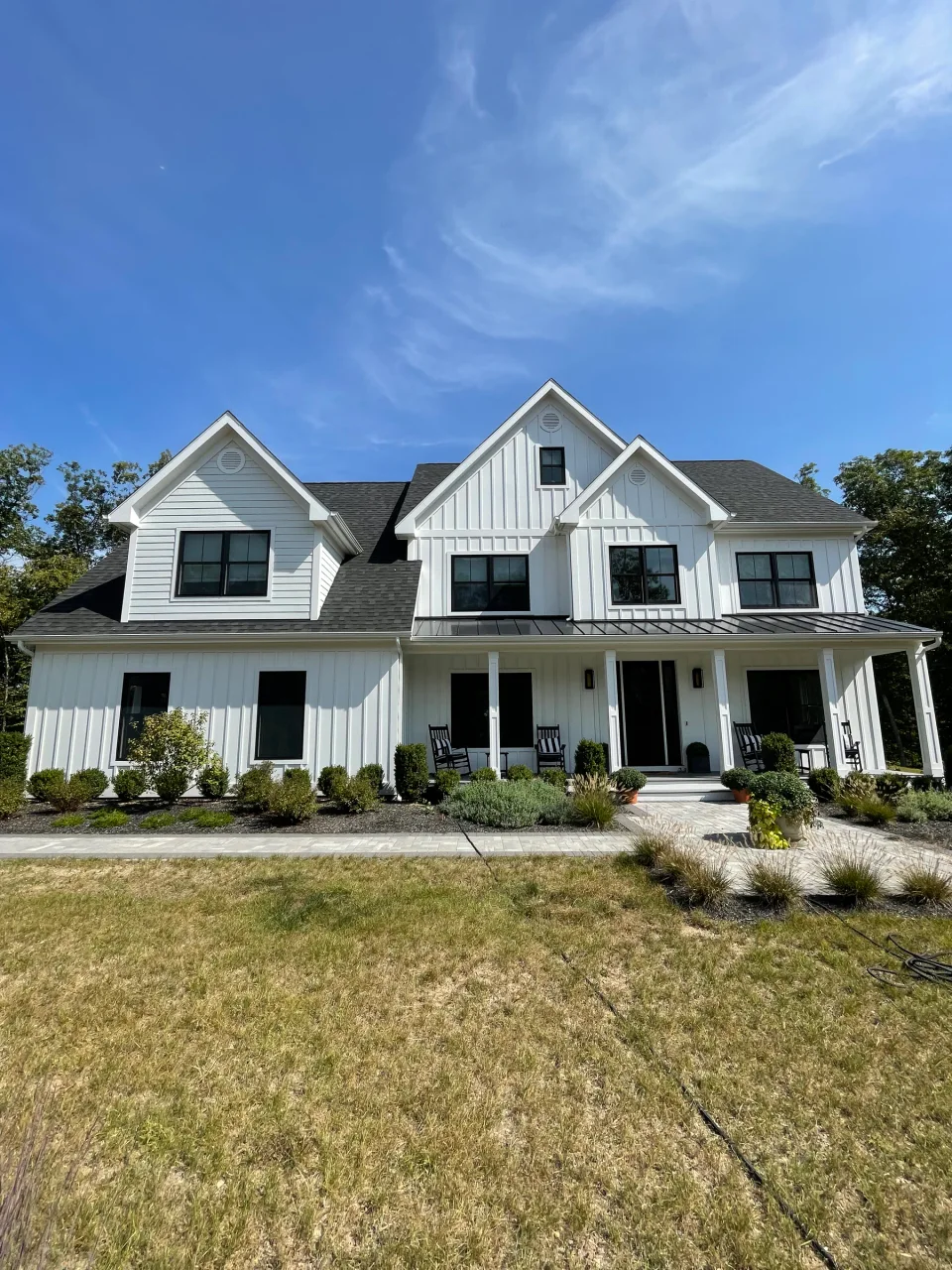White house with gabled rooflines, board-and-batten siding, window trim and a covered porch.